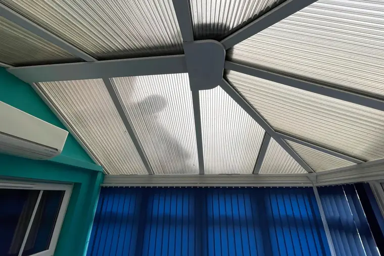 Ribbed polycarbonate roof sheets inside a conservatory with teal walls and blue blinds