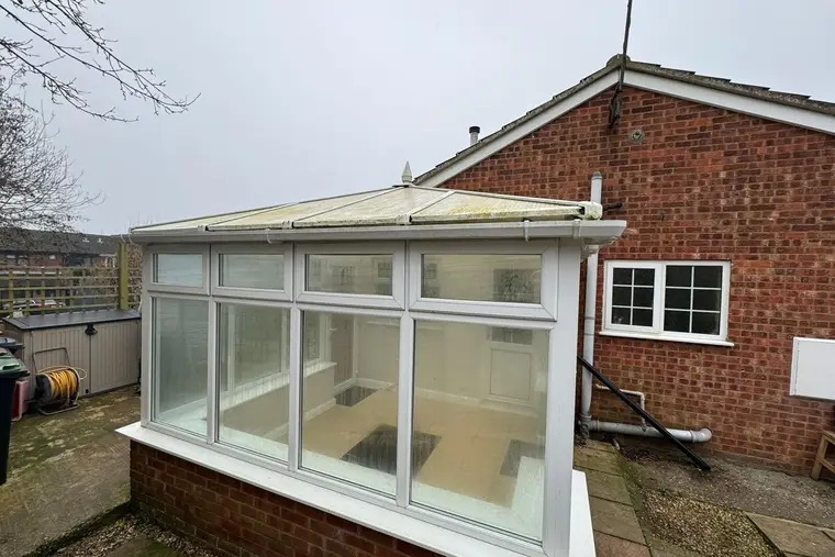 Conservatory with a discoloured translucent roof on the side of a brick bungalow