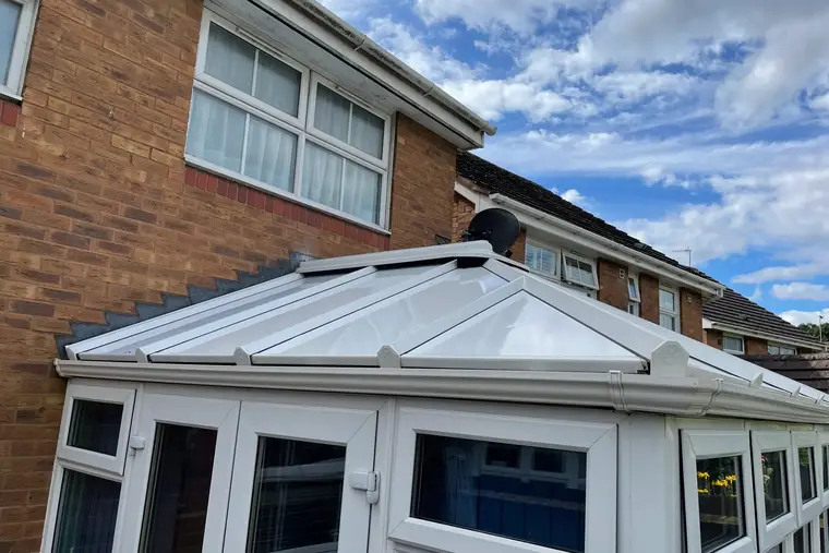 Smooth white insulated panel roof with capped glazing bars under a bright blue sky