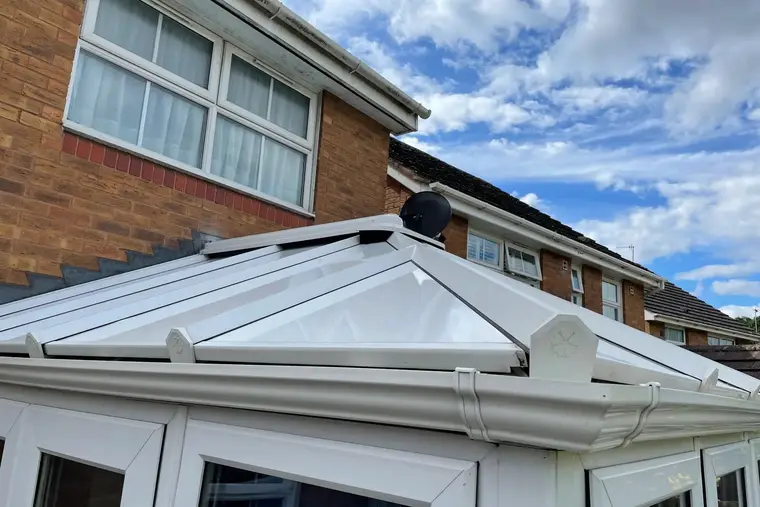 Close view of white insulated roof panels, glazing bar end caps and new guttering on a conservatory