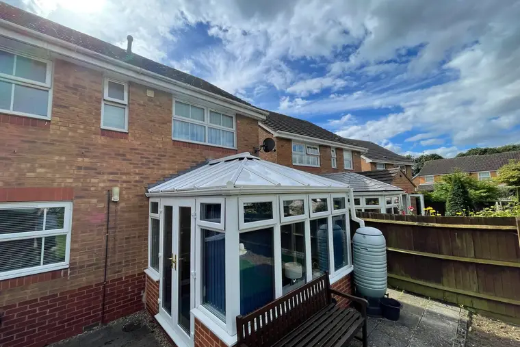 Wide view of a Victorian conservatory with a finished white panel roof at the back of a brick house