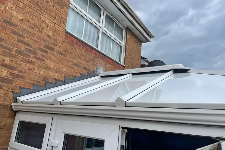 White insulated conservatory roof panels finished neatly against the brick wall of the house