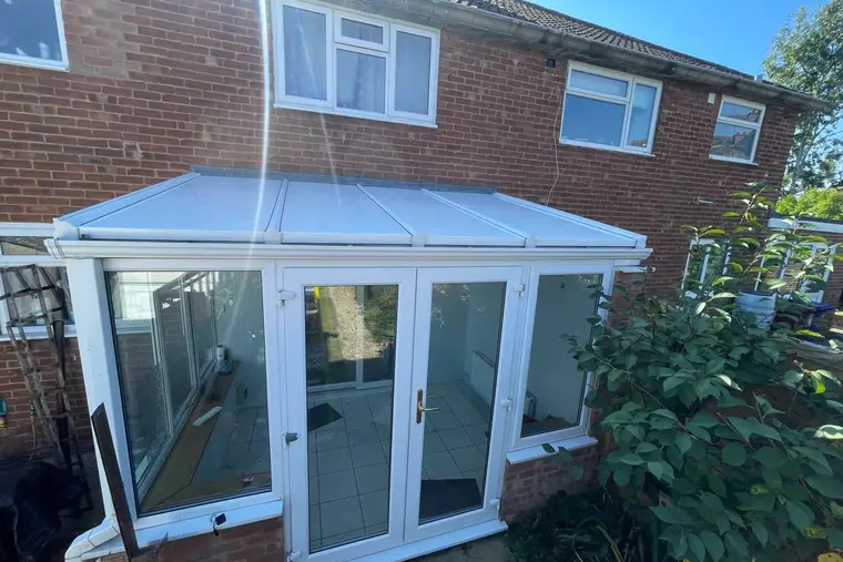 Lean-to conservatory with a new white insulated panel roof in afternoon sunshine