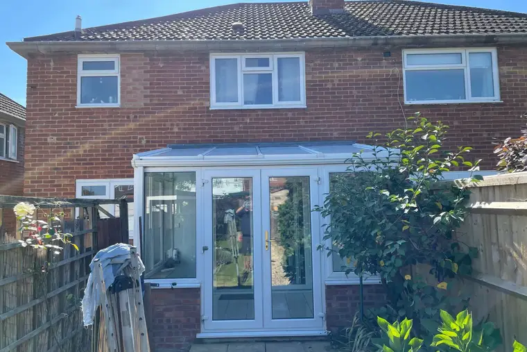 Rear of a red brick semi with a finished white panel roof on the lean-to conservatory
