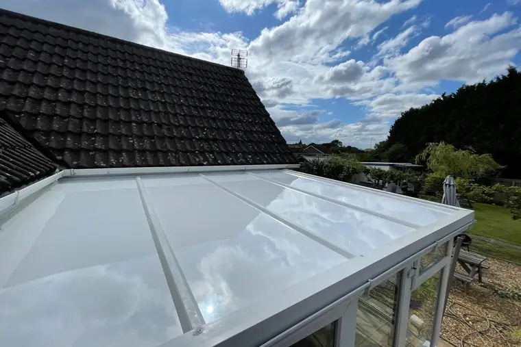 Glossy white insulated panel roof on a lean-to conservatory under a dramatic cloudy sky