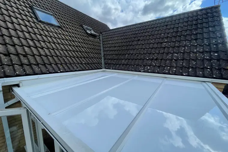 New white conservatory roof panels reflecting the clouds, set against a dark bungalow roof