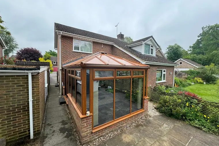 Oak-effect conservatory with a new copper-coloured insulated panel roof beside a garden