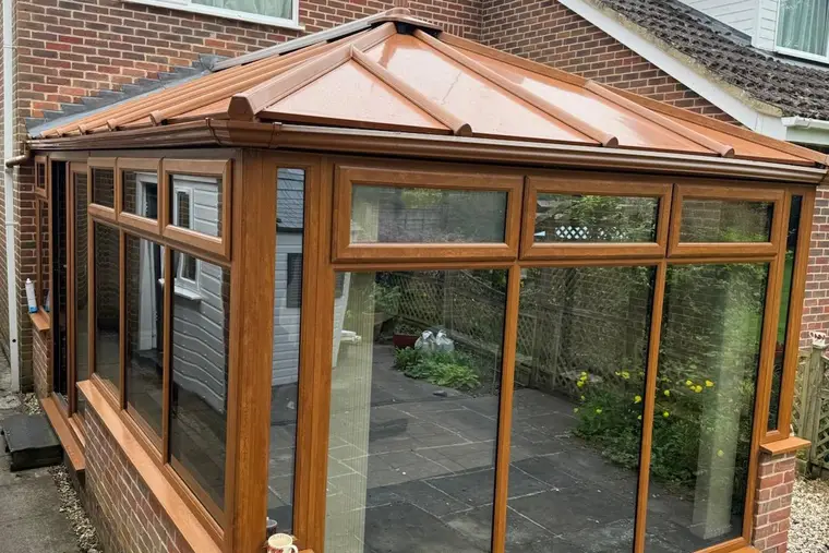 Side view of an oak-effect conservatory finished with a copper-coloured panel roof