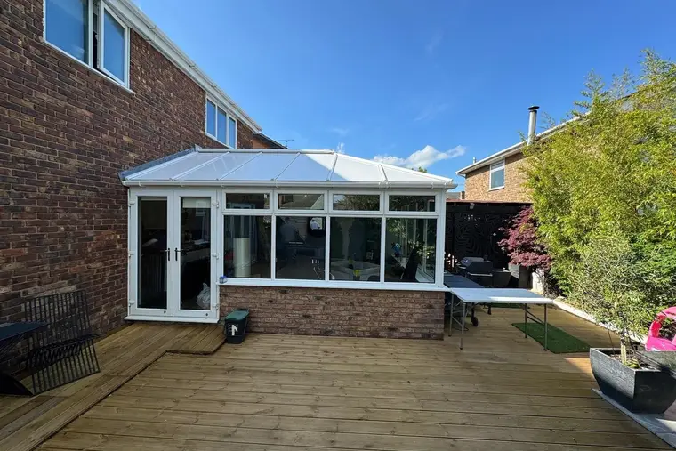 White conservatory with a finished insulated panel roof overlooking a timber deck