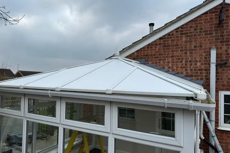 Finished white insulated panel roof on a conservatory beside a brick bungalow