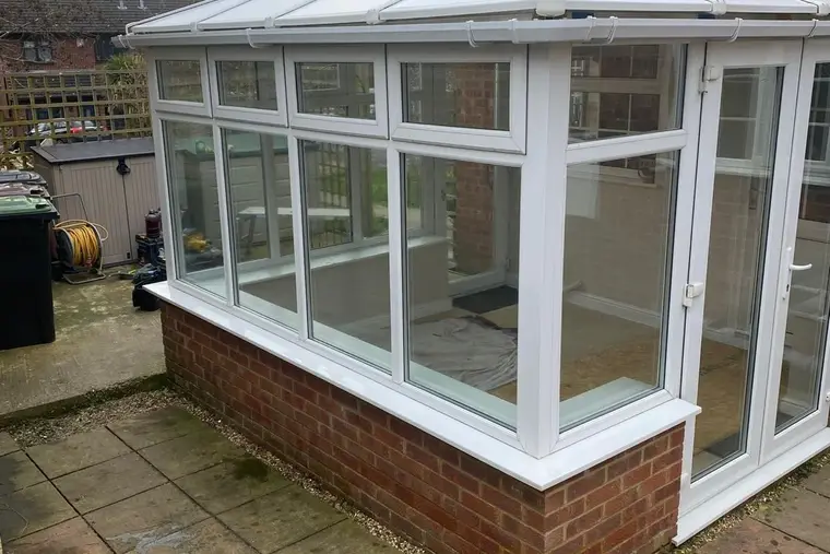 Corner view of a white conservatory with a new panel roof on a paved patio
