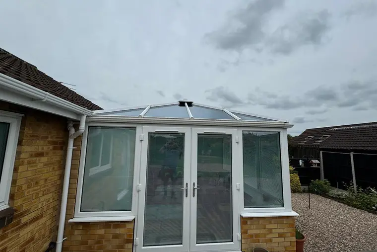 White conservatory with a new grey insulated panel roof on the back of a bungalow