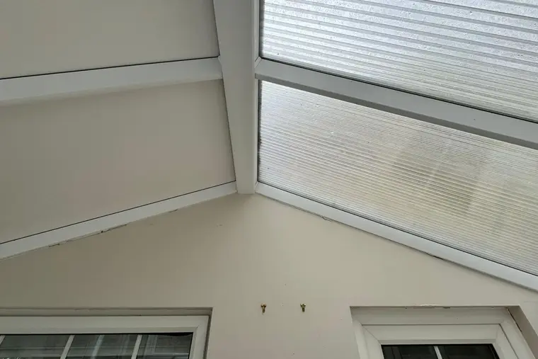 Inside a conservatory mid-installation, with old polycarbonate on one slope and new white panels on the next