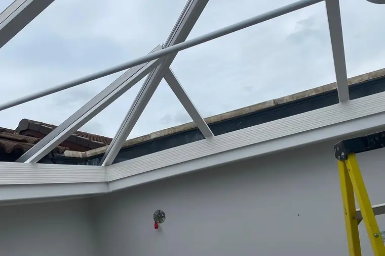 Glass removed from a conservatory roof, leaving the white frame open to the sky