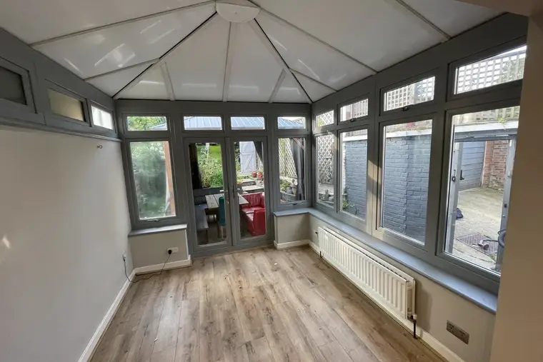 Grey-framed conservatory with a bright white insulated panel ceiling and oak-effect flooring