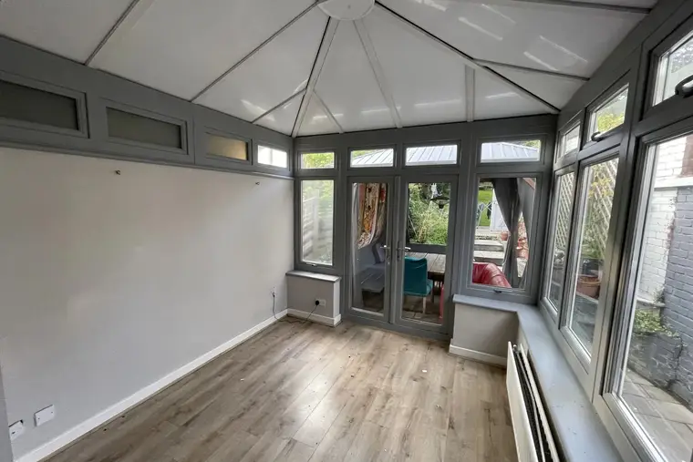 Empty grey-framed conservatory under a solid white insulated panel roof, ready to furnish