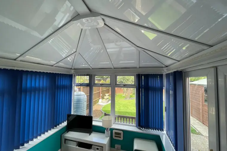 Teal-walled conservatory with blue blinds under a new white insulated panel ceiling
