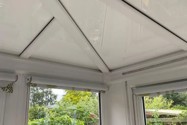 Corner of a conservatory with a white insulated panel ceiling above the garden windows