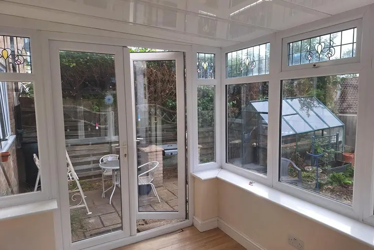 Bright conservatory with a glossy white panel ceiling and French doors to the patio